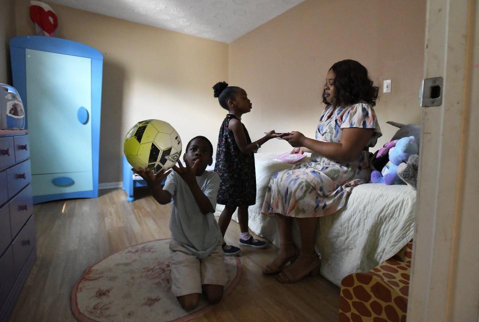 Kamari Phillips, 5, brings her mother Jasmine Jackson a book while her brother Keyon Phillips, 8, plays with his soccer ball in the family rental home in Jacksonville. Previously, Jackson and her three children had been homeless.