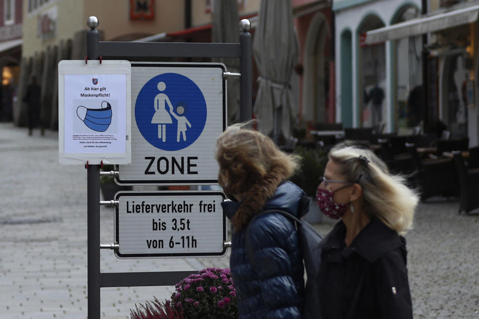 People pass a sign reading 'Face masks mandatory from here' in the deserted city of Berchtesgaden, Germany, Monday, Oct. 26, 2020. Authorities have posed the Berchtesgaden region under a lockdown since Oct. 20, 2020 due to a rising number of cases of the pandemic COVID-19 disease caused by the SARS-CoV-2 coronavirus in the district of Berchtesgadener Land. Local authorities in Bavaria's Rottal-Inn county, on the border with Austria, said Monday that the restrictions will begin at midnight. (AP Photo/Matthias Schrader)