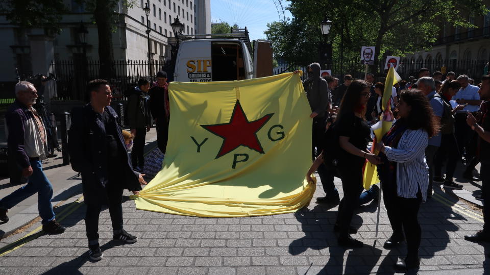 Demonstranten entrollen eine Flagge der kurdischen Volksverteidigungseinheiten YPG vor Downing Street 10 (Bild: Tobias Huch)