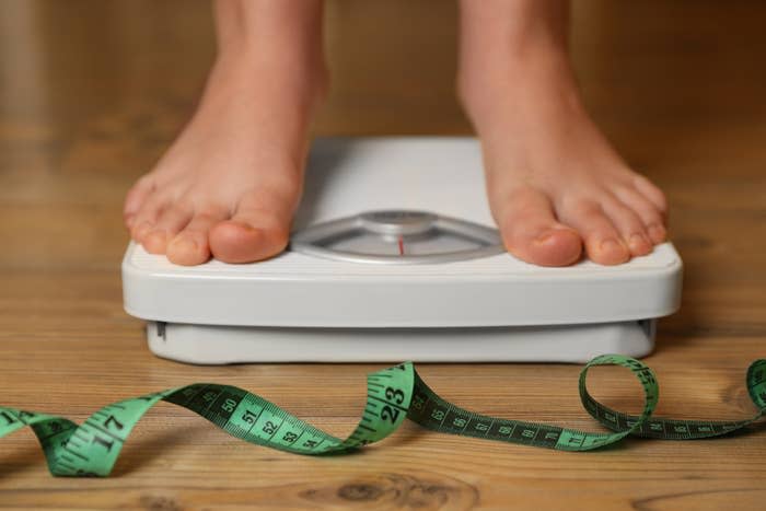 Bare feet on a bathroom scale with a measuring tape on the wooden floor