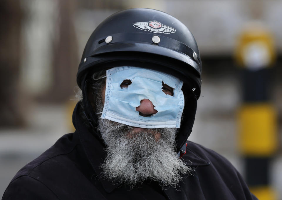 A man with a motorcycle helmet covers his face with a mask, as he watches municipal policemen order people to leave the corniche, or waterfront promenade, along the Mediterranean Sea, as the country's top security council and the government were meeting over the spread of coronavirus, in Beirut, Lebanon, in Beirut, Lebanon, Sunday, March 15, 2020. (AP Photo/Hussein Malla)