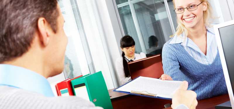 A bank teller hands a customer some paperwork.