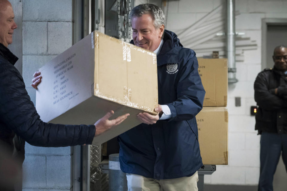 In this March 28, 2020 photo provided by the New York City Mayoral Photography Office, NYC Mayor Bill de Blasio helps load a carton containing some of 250,000 face masks into a truck on a loading dock at U.N. headquarters. The U.N. donated the masks for New York City's fight against the coronavirus. (Ed Reed/Mayoral Photography Office via AP)