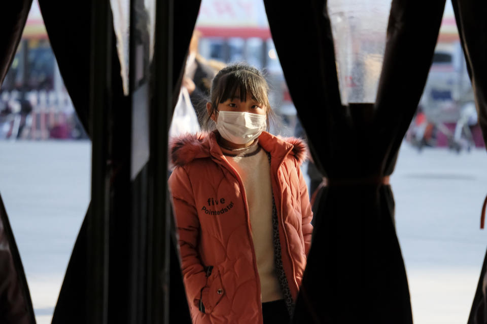 A girl wearing a face mask stands in the entrance to a shop in Wuhan in central China's Hubei Province, Friday, Jan. 31, 2020. The U.S. advised against all travel to China as the number of cases of a worrying new virus spiked more than tenfold in a week, including the highest death toll in a 24-hour period reported Friday. (AP Photo/Arek Rataj)