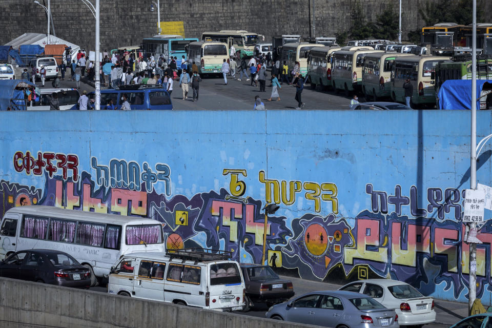 Passengers look for buses at a station, while vehicle drivers sit in traffic nearby, in the capital Addis Ababa, Ethiopia Friday, Nov. 6, 2020. Ethiopia's prime minister says airstrikes have been carried out against the forces of the country's Tigray region, asserting that the strikes in multiple locations "completely destroyed rockets and other heavy weapons." Coronavirus informational mural in Amharic reads "Keep your distance, everything will be alright soon". (AP Photo/Mulugeta Ayene)