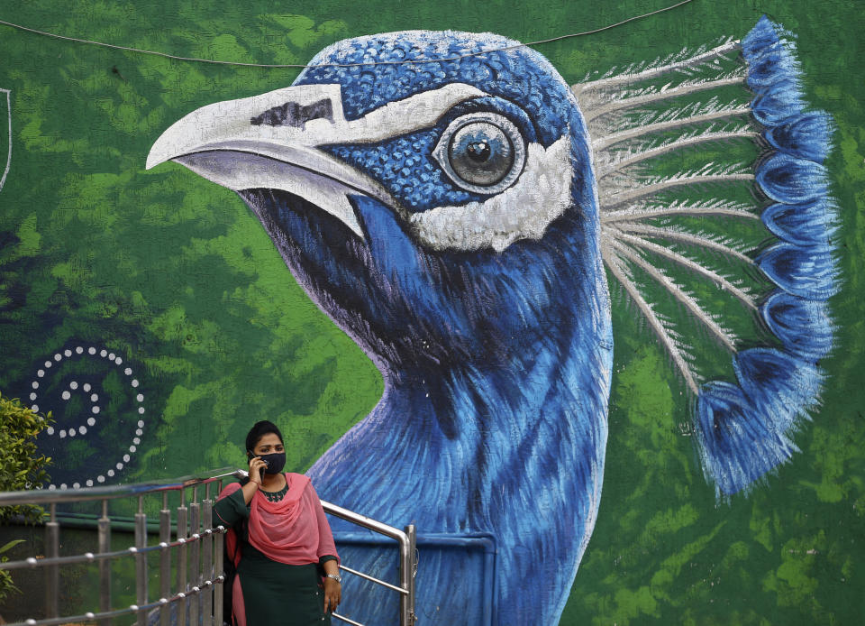 An Indian woman wearing face mask as a precaution against the coronavirus speaks on mobile phone standing in front of a Peacock graffiti on a wall in Hyderabad, India, Thursday, June 17, 2021. (AP Photo/Mahesh Kumar A.)