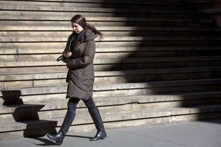 A woman checks her phone as she walks on a cold and windy day in New York's financial district February 13, 2015. REUTERS/Brendan McDermid