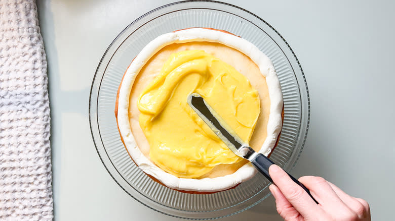 Spreading lemon curd filling on bright and sunny lemon lavender cake with buttercream border on serving platter