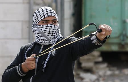 A Palestinian uses a sling shot at Israeli troops during clashes following an anti-Israel demonstration in solidarity with al-Aqsa mosque, in the West Bank city of Hebron November 21, 2014. REUTERS/ Mussa Qawasma