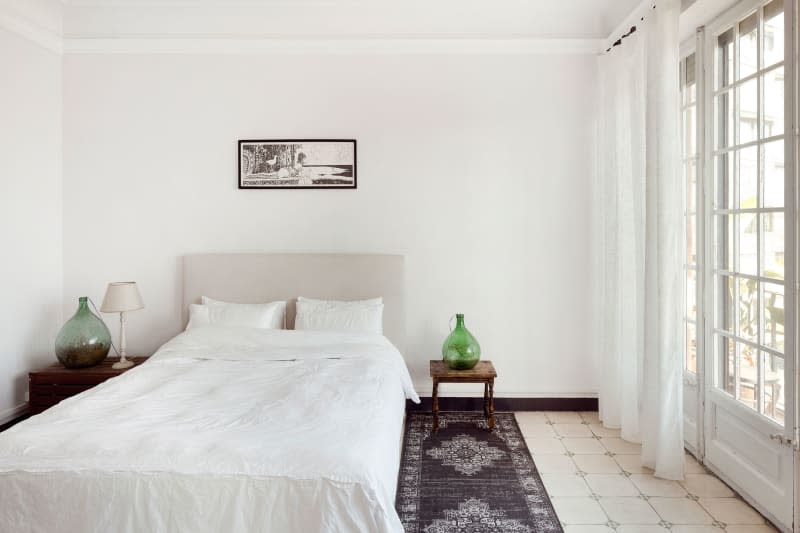 White bedding tops neutral bed in room with green glass accent vessels.