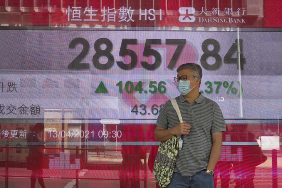 A man wearing a face mask walks past a bank's electronic board showing the Hong Kong share index at Hong Kong Stock Exchange in Hong Kong Tuesday, April 13, 2021. Asian shares were mostly higher on Tuesday with hopes growing for a global economic rebound despite worries over renewed surges in coronavirus cases. (AP Photo/Vincent Yu)