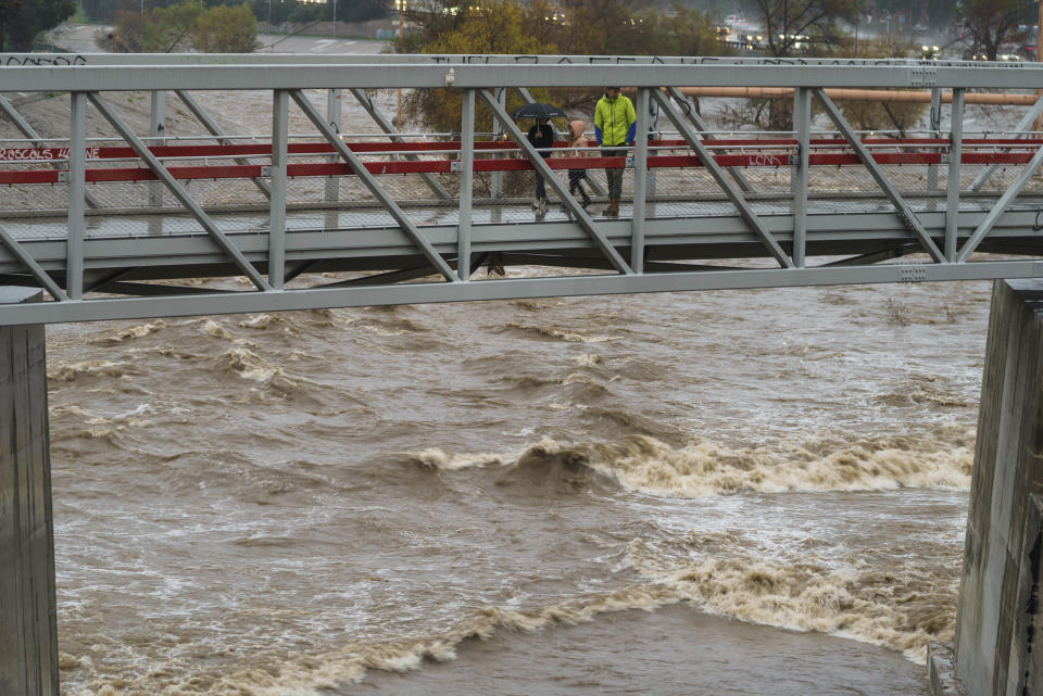 People cross a bridge over a swollen Los Angeles River in Los Angeles on Saturday, Jan. 14, 2023. Storm-battered California got more wind, rain and snow on Saturday, raising flooding concerns, causing power outages and making travel dangerous. (AP Photo/Damian Dovarganes)