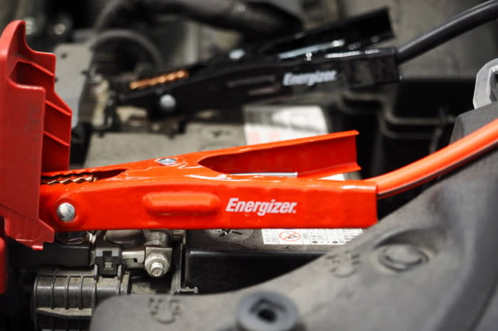 A set of jumper cables connected to a vehicle engine's battery terminal posts; (photo/Derek Mau)