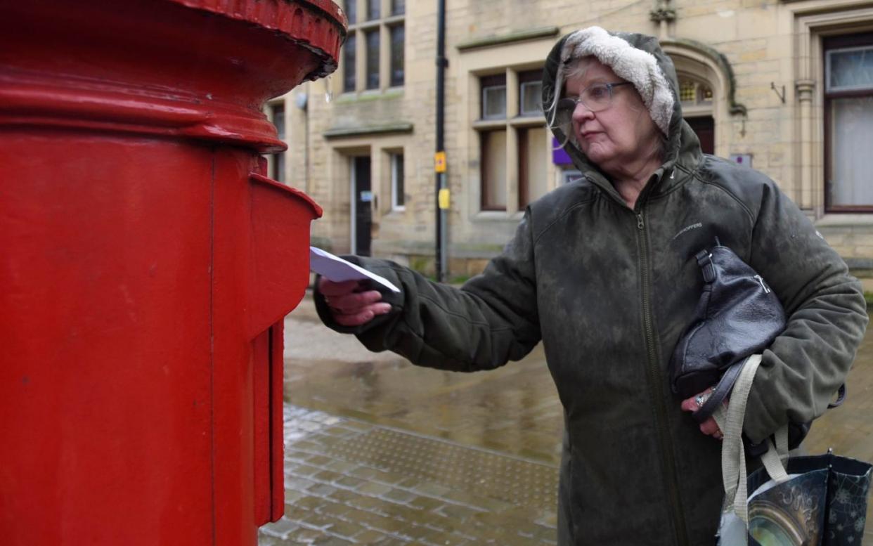 A woman posts a letter at a pillar box