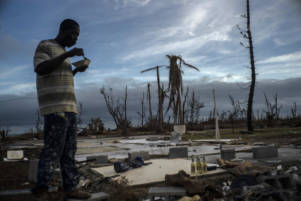 Jeffrey Roberts, 49, eats a plate of food while searching through the rubble of his relatives' home which was destroyed by Hurricane Dorian in Pelican Point, Grand Bahama, Bahamas, Saturday, Sept. 14, 2019. The death toll from the hurricane stands at 50 and the number of missing at an alarming 1,300 people, although officials caution the list is preliminary and many people could just be unable to connect with loved ones. (AP Photo/Ramon Espinosa)