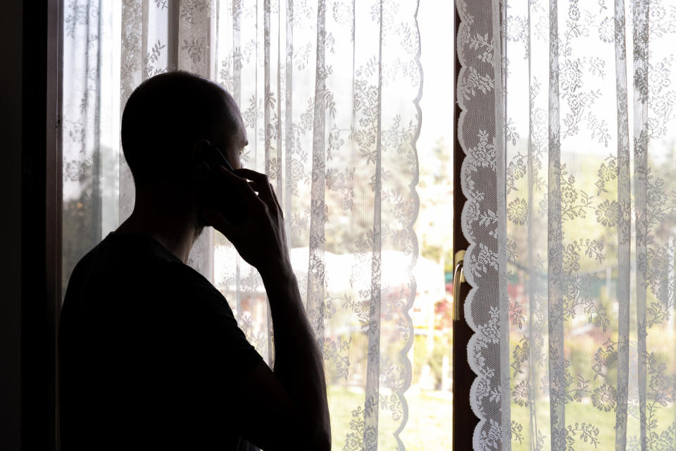 Someone alone in a room, looking out the window while talking on the phone