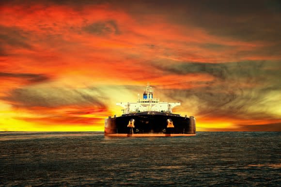 A tanker at sea with an orange sky at sunset.