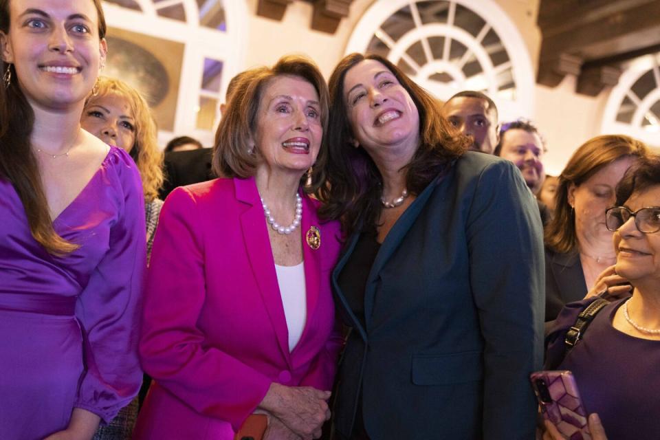 Two smiling women stand together closely in a crowd