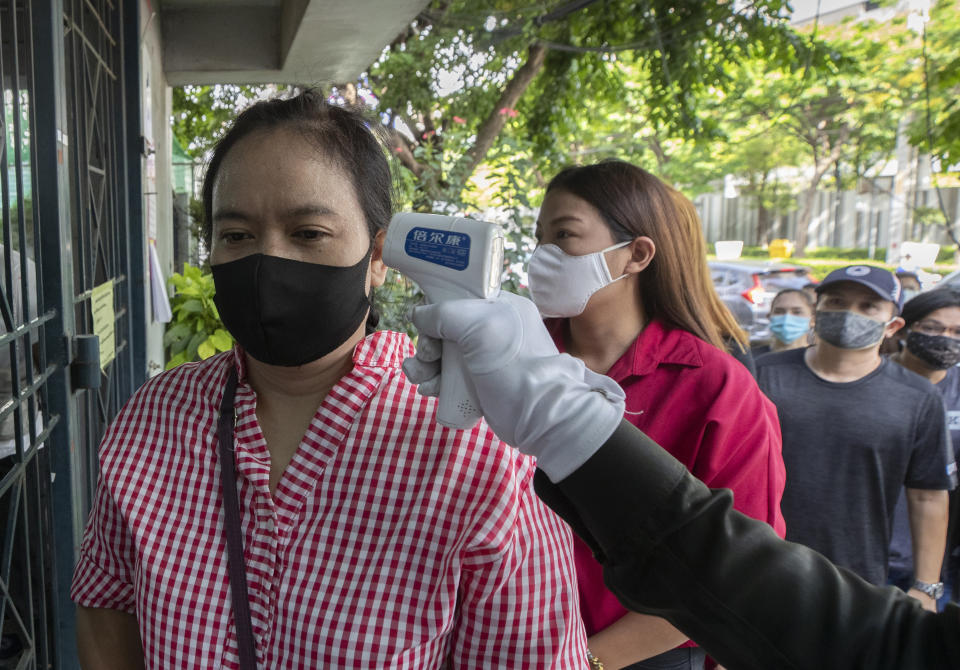 An officer checks the temperature of Wannapa Kotabin, a 38-year-old kitchen assistant at an Italian restaurant, in front of Social Security office for claim unemployment benefit in Bangkok, Thailand, Thursday, June 4, 2020. The government ordered all restaurants closed in March to combat the spread of the coronavirus, and Wannapa hasn't worked since. That's the harsh truth facing workers laid off around the world, from software companies in Israel to restaurants in Thailand and car factories in France, whose livelihoods fell victim to a virus-driven recession that's accelerating decline in struggling industries and upheaval across the global workforce. (AP Photo/Sakchai Lalit)