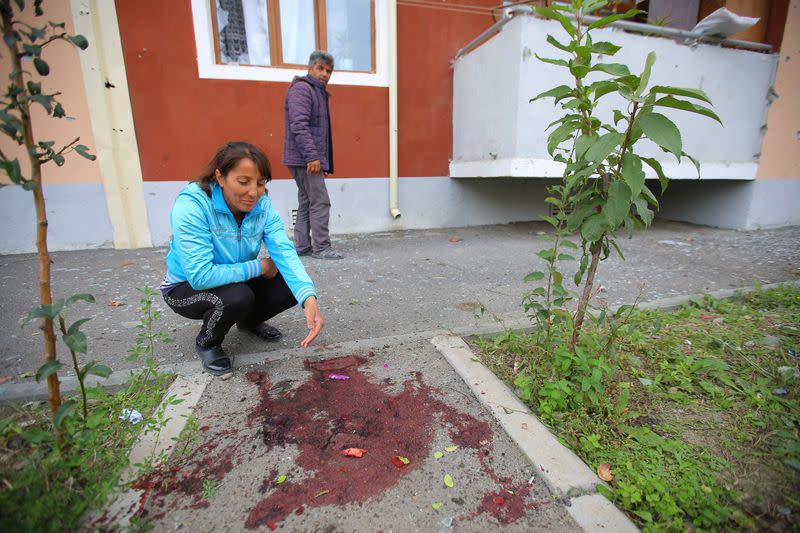 A woman sits next to a blood stain after what locals said was shelling in Tartar district