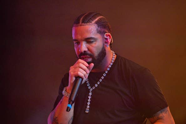 Music artist performing on stage with microphone, wearing a simple black shirt and necklaces