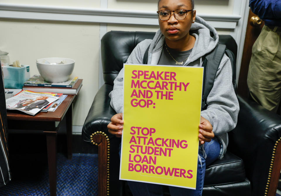 A man holding a sign that says, "Stop Attacking Student Loan Borrowers"