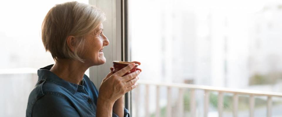 retirement age woman drinking coffee from a mug looking out the window