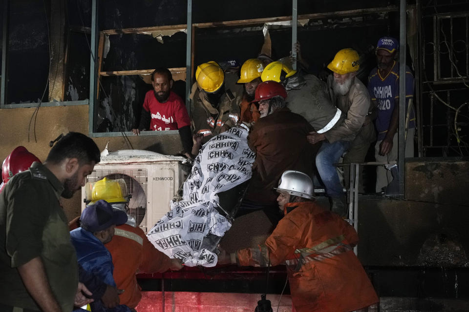 Firefighters and rescue workers recover a body from a burnt multi-story commercial building in Karachi, Pakistan, Wednesday, Dec. 6, 2023. A massive fire broke out Wednesday in a multi-story commercial building in Pakistan's largest southern port city of Karachi, killing a number of people and damaging several shops, police and rescue officials said. (AP Photo/Fareed Khan)