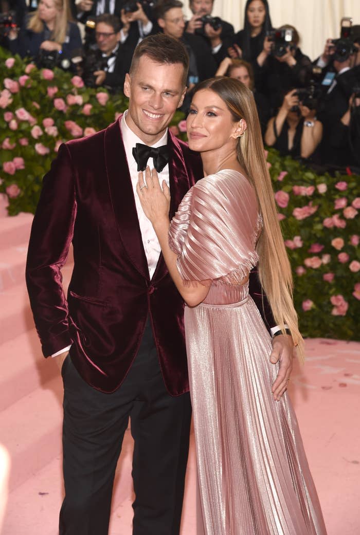 Tom Brady and Gisele Bündchen posing together; he's in a velvet suit and she's wearing a metallic gown