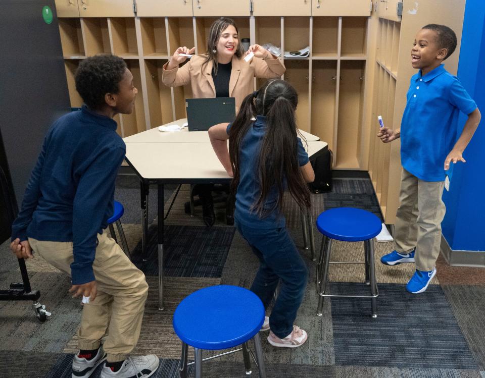 Second-graders Keon Viverette, left to right, Daniela Nieves and Ivory Donson play a literacy game with tutor Grace Martin during a Circle City Readers tutoring session Thursday, Nov. 9, 2023, at Vision Academy at Riverside in Indianapolis. The students are hopping to count each syllable in a given word.