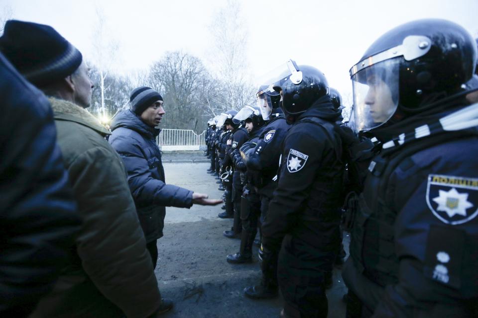 Protesters, who planned to stop buses with passengers from the Ukrainian aircraft chartered by the Ukrainian government for evacuation from the Chinese city of Wuhan, speak to Ukrainian riot police blocking the road outside Novi Sarzhany, Ukraine, Thursday, Feb. 20, 2020. Several hundred residents in Ukraine's Poltava region protested to stop officials from quarantining the evacuees in their village because they feared becoming infected. Demonstrators put up road blocks and burned tires, while Ukrainian media reported that there were clashes with police, and more than 10 people were detained. (AP Photo/Efrem Lukatsky)