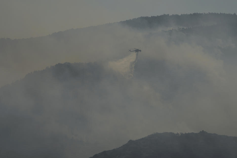 A helicopter drops water during a wildfire near Tatoi, in northern Athens, Greece, Saturday, Aug. 7, 2021. Wildfires rampaged through massive swathes of Greece's last remaining forests for yet another day Saturday, encroaching on inhabited areas and burning scores of homes, businesses and farmland. (AP Photo/Petros Karadjias)