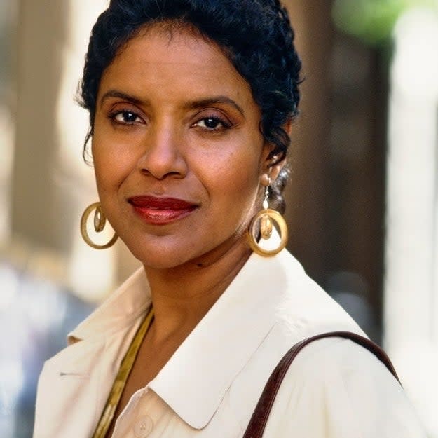 Phylicia posing for the camera, wearing a buttoned shirt, hoop earrings, and carrying a shoulder bag