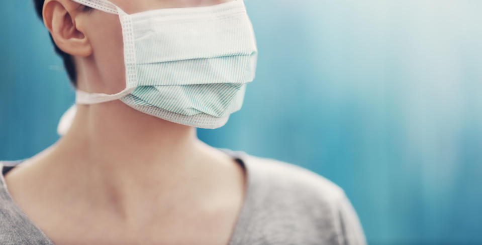 young woman in medical face protection mask indoors on blue background. Sick person