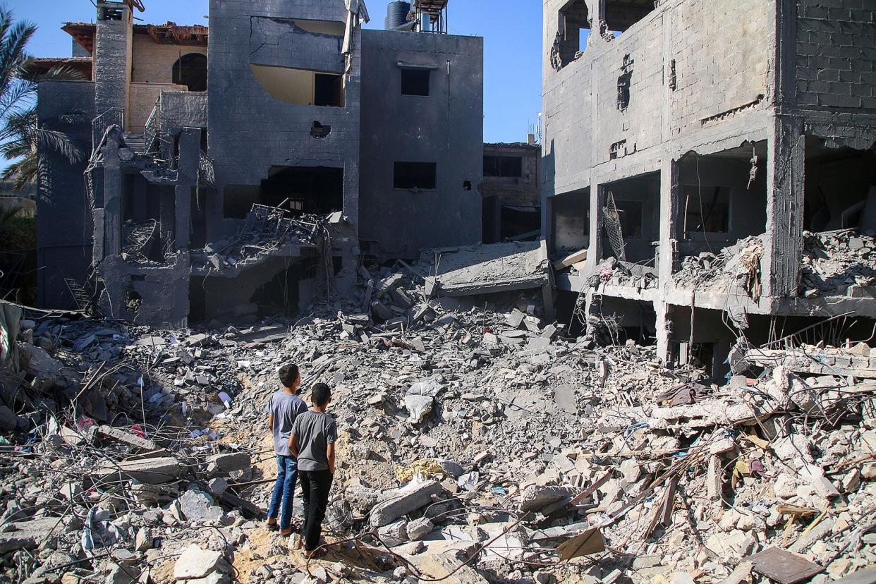 Two people stand among the rubble of buildings.