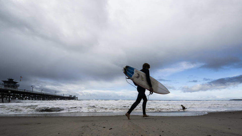 A surfer heads to the water as storms move through the area in San Clemente, Calif., on Monday, Dec. 12, 2022. (Paul Bersebach/The Orange County Register via AP)