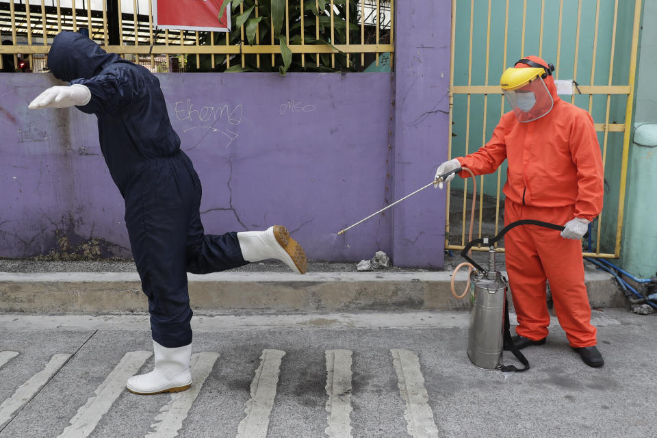 A government worker wearing a protective suit disinfects the shoes of his colleague outside a COVID-19 testing site to curb the spread of the coronavirus in Quezon city, Philippines on Thursday, April 29, 2021. The Philippines is extending an already monthlong lockdown by two weeks as the country's worst coronavirus infection spike starts to ease but remains alarming. (AP Photo/Aaron Favila)