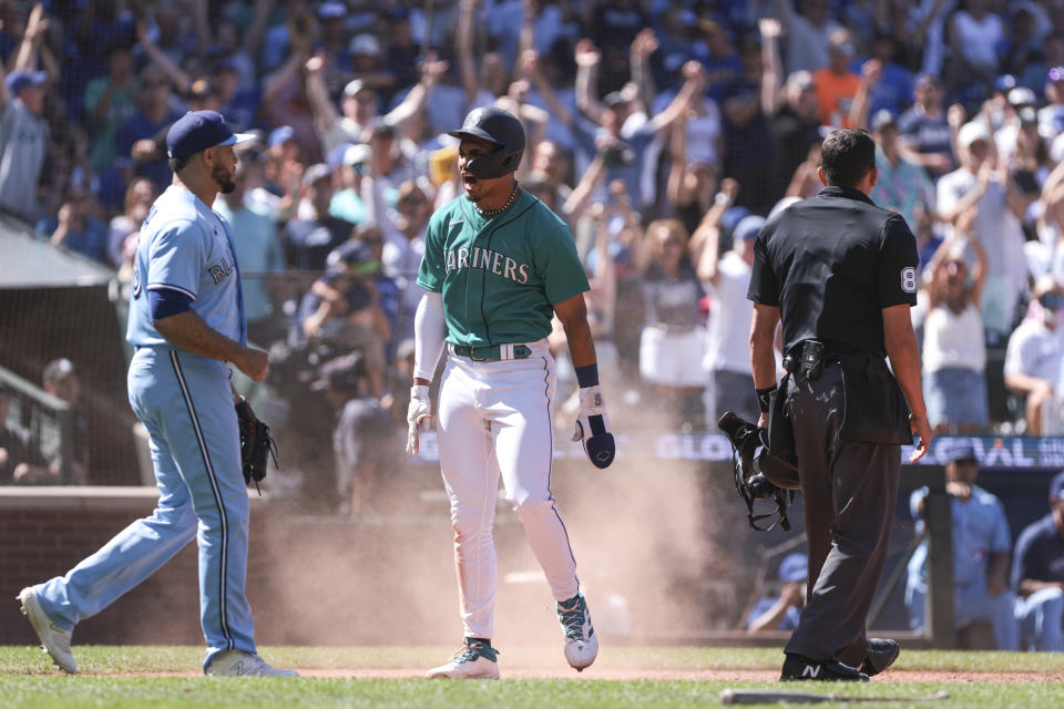 Seattle Mariners' Julio Rodriguez, center, celebrates after a play at home plate as Toronto Blue Jays relief pitcher Yimi Garcia, left, looks on during the seventh inning of a baseball game, Saturday, July 22, 2023, in Seattle. (AP Photo/Jason Redmond)