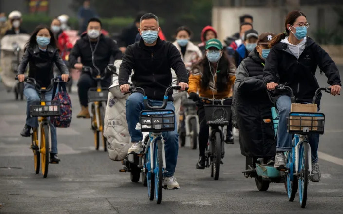 Commuters wearing face masks ride bicycles along a street in the central business district in Beijing - Mark Schiefelbein/AP