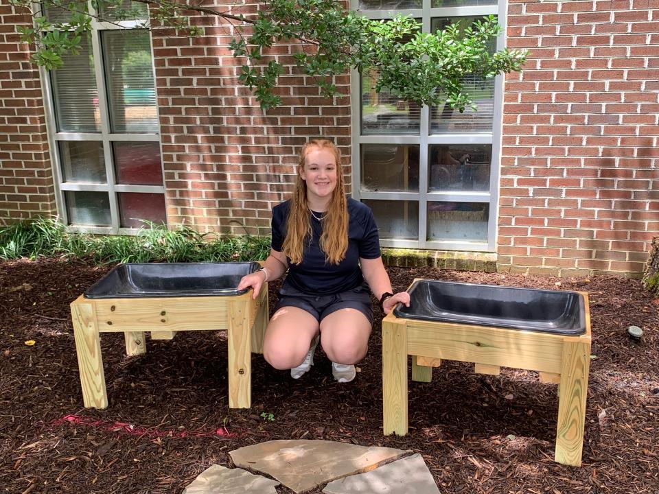 Ally Bush sits next to the two playground garden tables she helped build for the Trinity Learning Center at First Farragut United Methodist Church as part of a project that helped her receive a Girl Scout Gold Award.