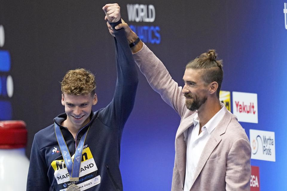 Swimming great Michael Phelps, right, hold up the arm of Leon Marchand, of France, during a medal ceremony for the men's 400m individual medley final at the World Swimming Championships in Fukuoka, Japan, Sunday, July 23, 2023. Marchand won gold setting a new world record, breaking Phelps' 2008 record. (AP Photo/David J. Phillip)