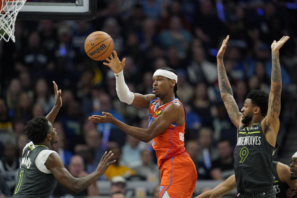 Oklahoma City Thunder guard Shai Gilgeous-Alexander passes while defended by Minnesota Timberwolves guarda Anthony Edwards, left, and Nickeil Alexander-Walker (9) during the first half of an NBA basketball play-in tournament game Friday, April 14, 2023, in Minneapolis. (AP Photo/Abbie Parr)