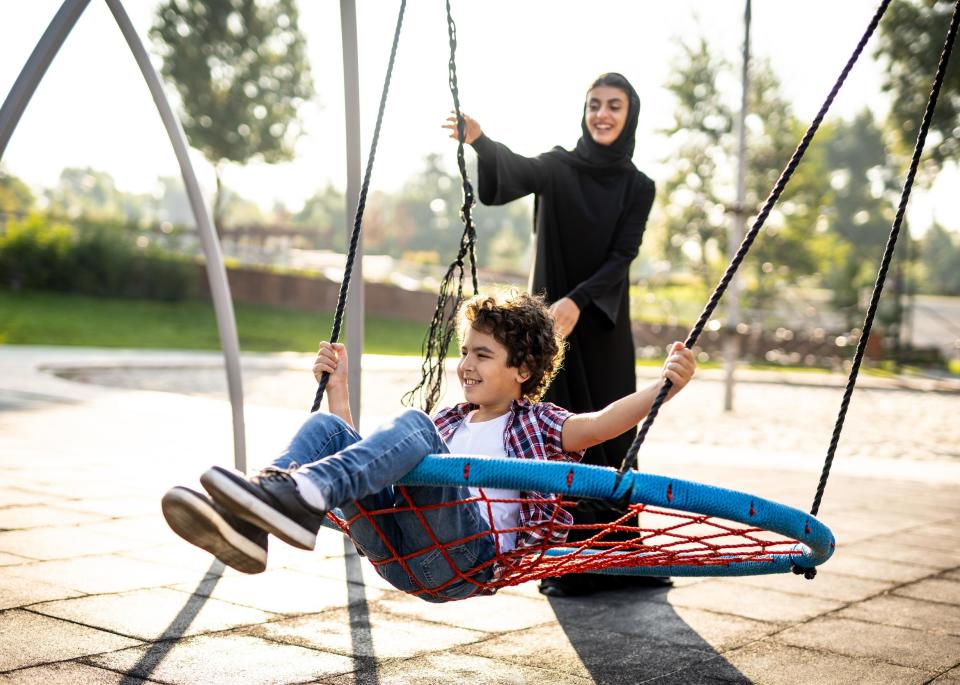 Woman pushing child on swing on playground.