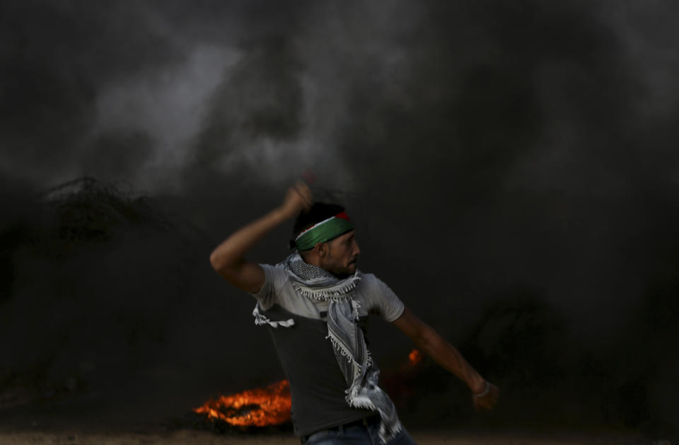 A protester hurls stones while others burn tires near the fence of the Gaza Strip border with Israel, east of Khan Younis, southern Gaza Strip, Friday, Oct. 19, 2018. (AP Photo/Adel Hana)