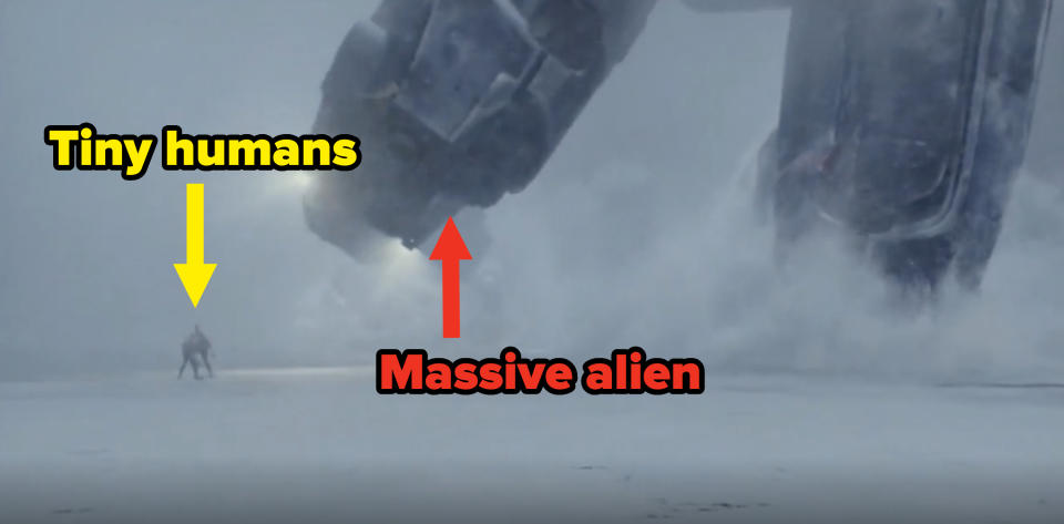 A huge alien's feet towering over two human beings