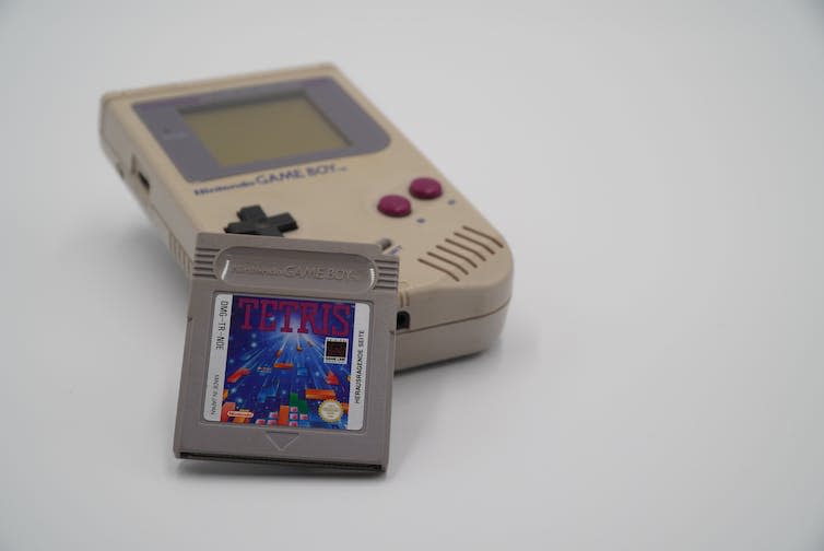 A grey square Tetris cartridge propped up against a Nintendo Game Boy console