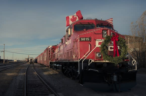 Train led by red locomotive with Canadian and American flags and a green wreath with red bow.