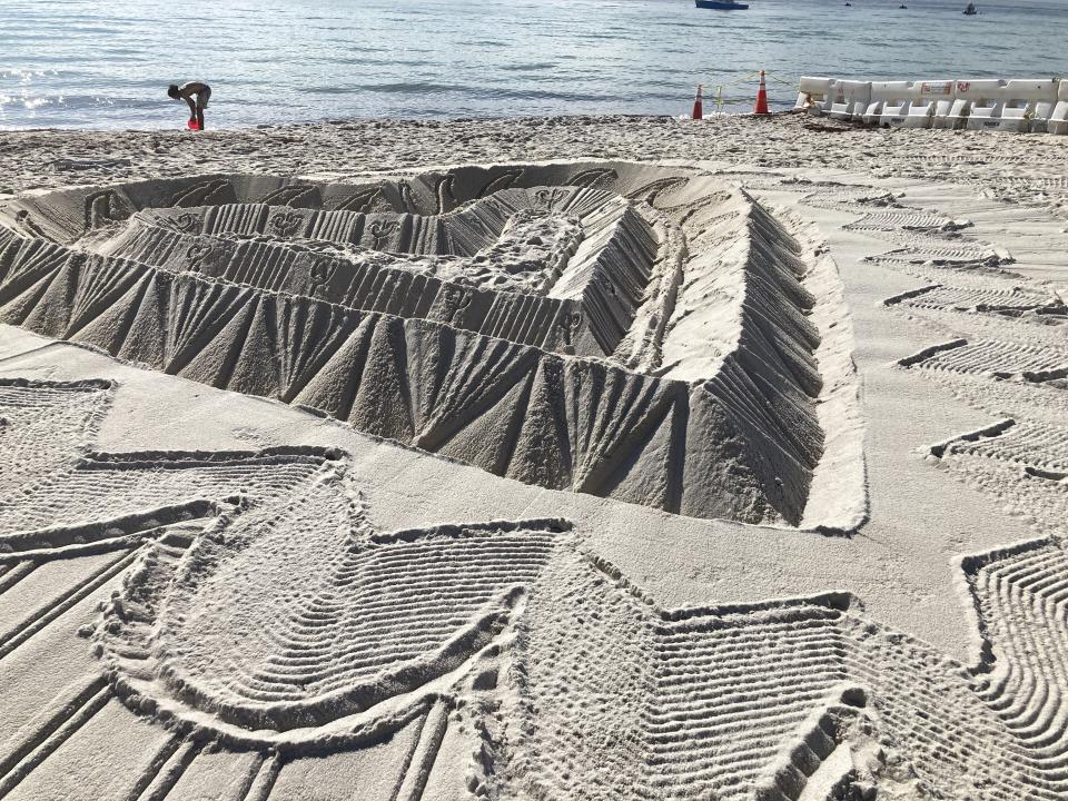Sand sculptors adorns the beach beside the area that is closed for search and rescue operations at the partially collapsed Champlain Towers South condo building, Friday, July 2, 2021, in Surfside, Fla. (AP Photo/Terry Spencer)
