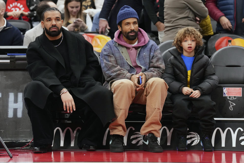 Drake, left, sits with his son Adonis Graham, right, before the Toronto Raptors take on the Phoenix Suns in an NBA basketball game in Toronto on Wednesday, Nov. 29, 2023. (Chris Young/The Canadian Press via AP)