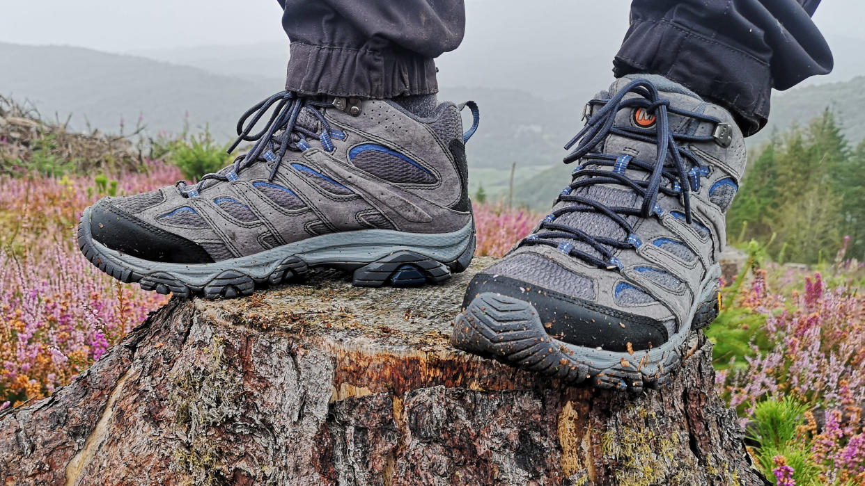  Person's feet standing on rock wearing Merrell Moab 3 Mid GTX hiking boots 